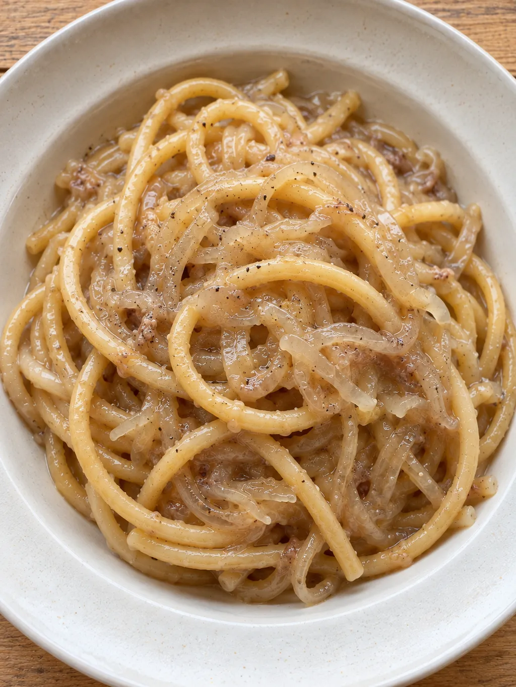 Bigoli con salsa chiara di cipolle e acciughe, completati con pepe nero