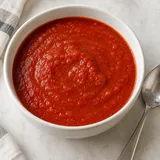 Una ciotola bianca di sugo di pomodoro con un cucchiaio accanto.
