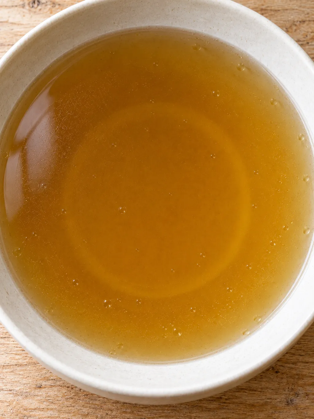 Brodo di manzo trasparente dal colore dorato in una scodella avorio