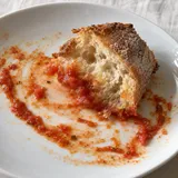 Un piccolo boccone di pane appoggiato nel sugo di pomodoro rimasto su un piatto bianco.