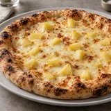Pizza con mozzarella e piccoli pezzi di ananas su un piatto bianco.