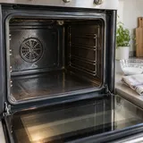 Forno spento con porta aperta, una ciotola di pasta di bicarbonato e un panno sul piano vicino.
