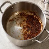 Pentola in acciaio con residui scuri di sugo sul fondo interno.