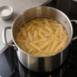 Pentola con penne immerse nell’acqua e una piccola ciotola di sale accanto.